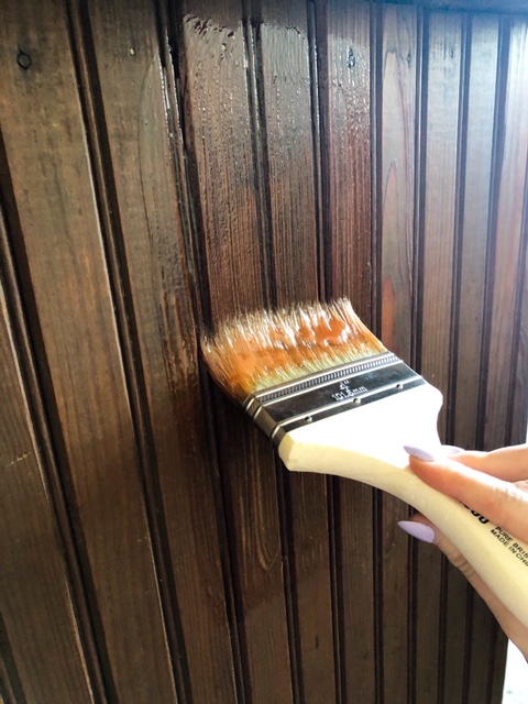 paintbrush with citristrip on it applying to dark wood in order to strip to original color and whitewash