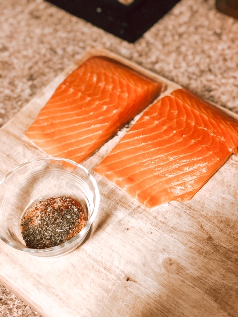 two filet of raw salmon and a small glass bowl of seasoning