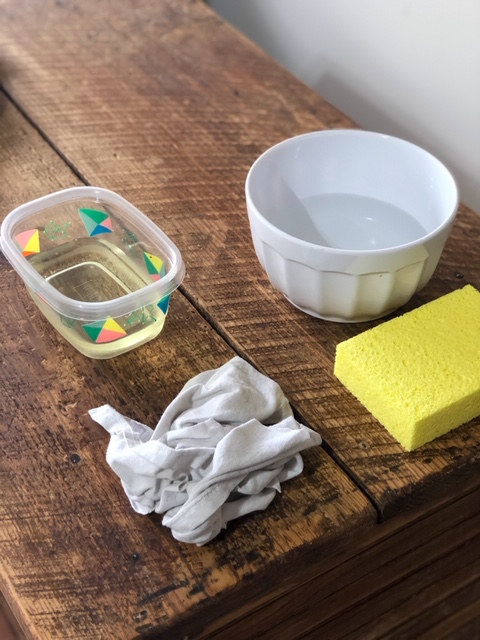 a Tupperware filled with bleach and a bowl filled with white vinegar and water to be used to whitewash dark wood kitchen island