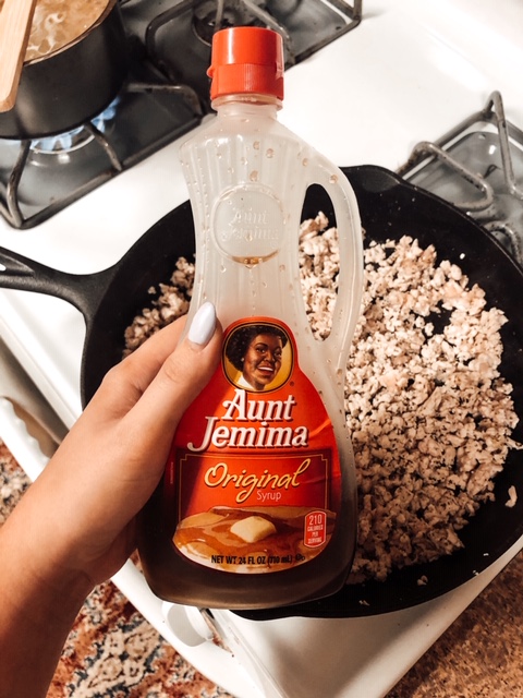 hand holding aunt jemima syrup over a skillet with ground turkey meat 