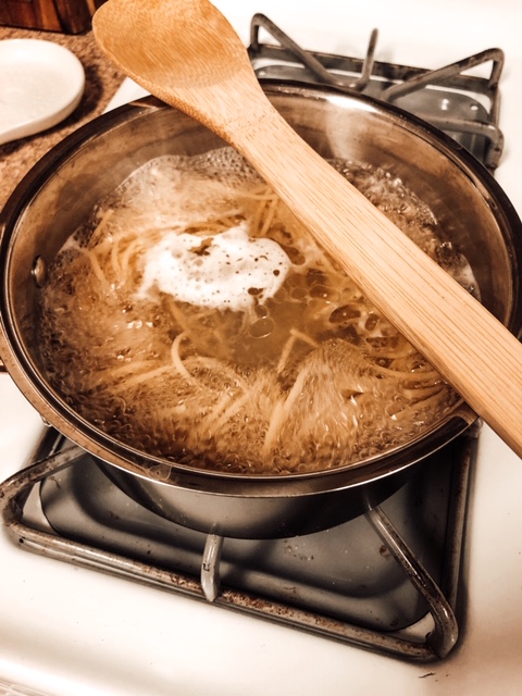 black pot with boiling water and noodles cooking with a wooden spoon over the pot 