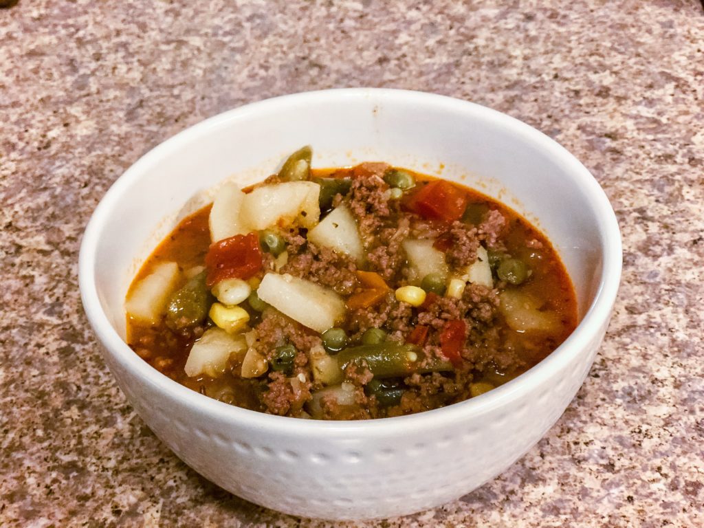 hearty hamburger and vegetable soup in a white bowl